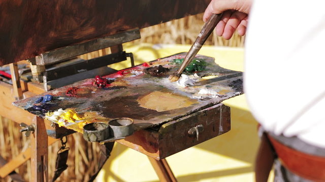 painter mixes with the brush colors in his palette