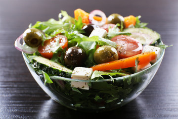 Greek salad in glass dish on wooden table background