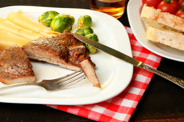 Roasted meat and vegetables on plate, on wooden table
