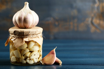 Canned garlic in glass jar on color wooden background