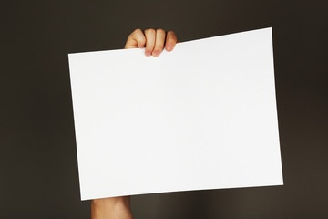Fototapeta premium Blank sheet of paper in male hand on dark background