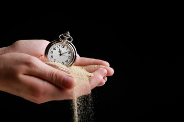 Silver pocket clock in hands and sand flowing away