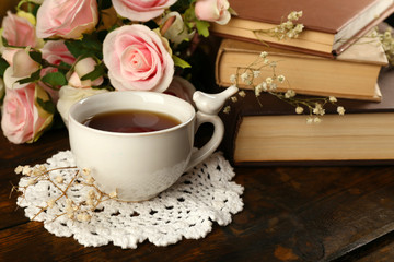Cup of tea with books and flowers on wooden background