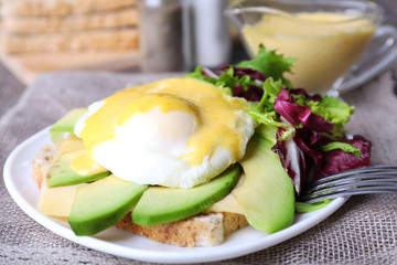 Toast with egg Benedict and avocado on plate on table close up