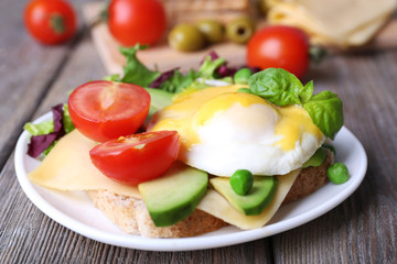 Toast with egg Benedict and avocado on plate on wooden table