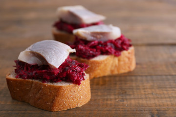 Herring with beets on rye toasts on wooden background