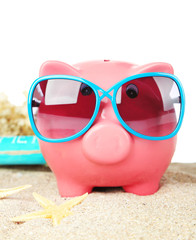 Piggy bank with sunglasses on sand, on white background