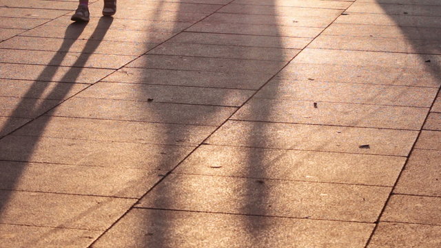 long shadows of people walking on the sidewalk at sunset
