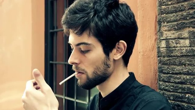 Pensive guy leaning against wall and waiting for someone and smoke a cigarette