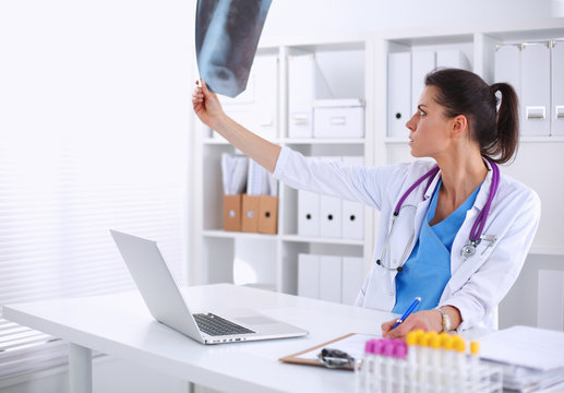 Young female doctor studying x-ray image sitting on the desk