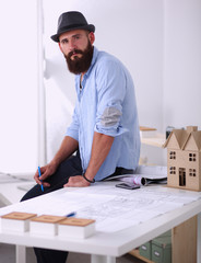 Portrait of male designer in hat with blueprints at desk