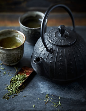 A cast iron tea pot and green tea in ceramic cups