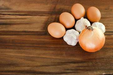 Eggs, garlic, onion on a brown wooden table