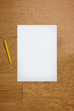 Pen and blank paper sheet on a worn wooden table