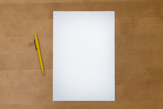 Pen and blank paper sheet on a wooden table