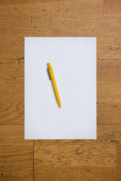 Pen on a blank paper sheet on a worn wooden table