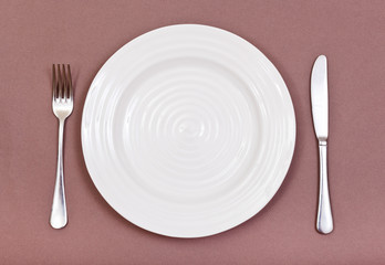 top view of white plate, fork, knife set on brown