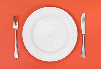 top view of white plate, fork, knife on red