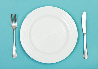 top view of white plate, fork, knife on green