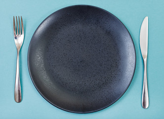 top view of black plate, fork, knife set on green