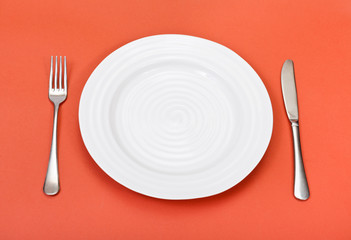 above view of white plate, fork, knife on red