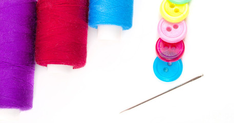 Needle, thread and buttons of different colors on white backgrou