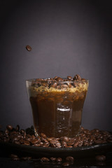 Coffee beans and coffee splashing in a glass on a dark backgroun