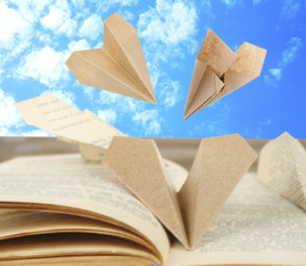 Origami airplanes on book on sky bakground