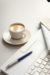 A cup of coffee, paper and a pen on a laptop