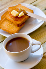 Breakfast time: cup of milky coffee, rusks with butter and jam