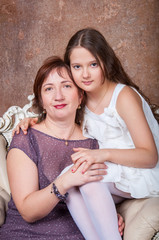 Мама и дочка сидят около елки обнимаются и юлыбаются