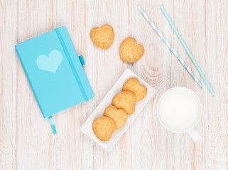 Cup of milk, heart shaped cookies and notepad