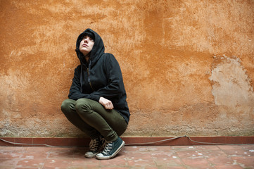 Dark young woman sad crouched near urban wall portrait