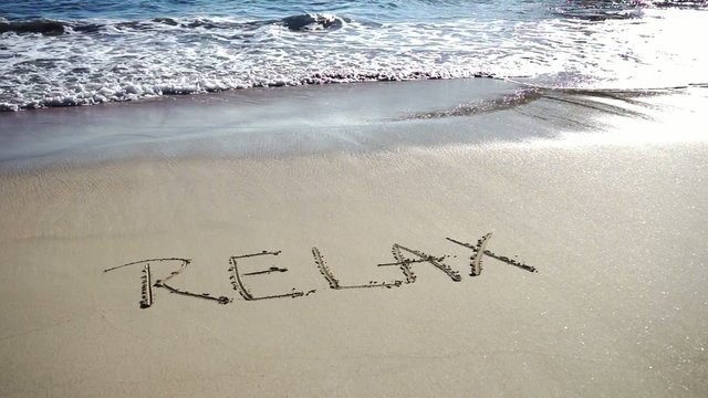 the word relax written on a sandy beach
