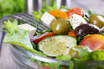 Greek salad in glass dish with fork on wooden table background