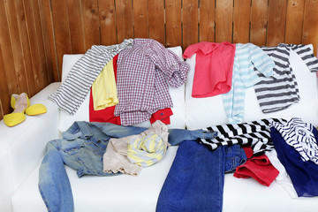 Messy clothing on white sofa, on wooden planks  background
