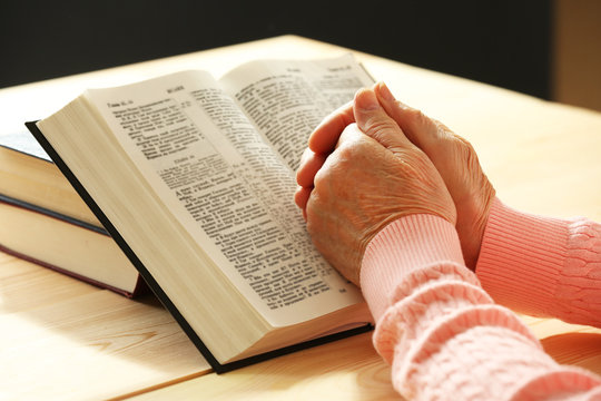Hands of old woman with Bible on table and dark background