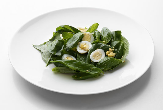 Salad with quail egg and basil in plate isolated on white