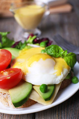 Toast with egg Benedict and avocado on plate on wooden table
