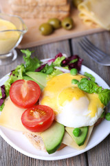 Toast with egg Benedict and avocado on plate on wooden table