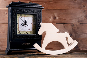 Retro clock with decorative horse on table on wooden background