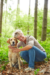 Lächelnde Seniorin mit Hund im Wald