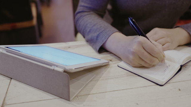 Woman taking notes in notebook, touch pad nearby