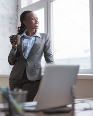 Businesswoman standing near window and drinking coffee