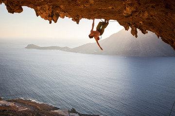 Rock climber climbing along roof in cave at sunset