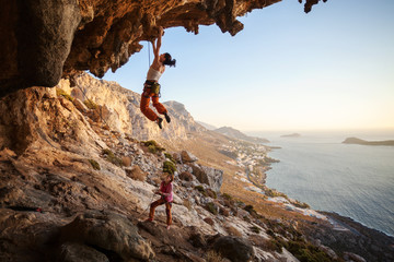 Young woman climbing on cliff, female partner belaying