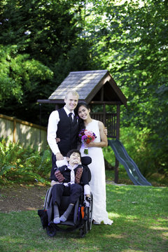 Interracial bride and groom standing with her disabled little bo