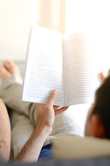 Naklejka premium A man reading book while lying on the couch