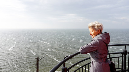 Woman looking over het IJselmeer from the lighthouse in Urk, an historic fishing village in the Netherlands - obrazy, fototapety, plakaty
