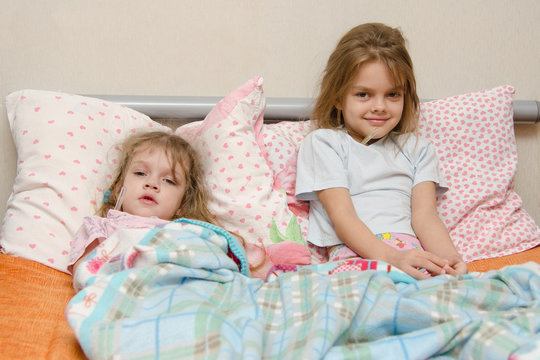 Two girls sick in bed with a thermometer